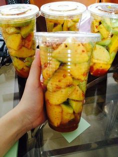 a person holding up a plastic cup filled with sliced fruit on top of a table