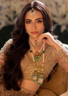 a beautiful woman in a gold and green outfit sitting on a couch with her hand near her face