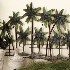 three metal palm trees are on display in front of a white wall with potted plants