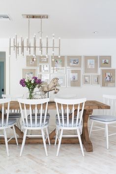 a dining room table with white chairs and pictures on the wall