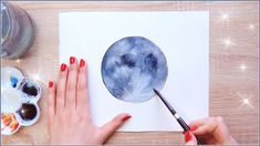 a woman's hand is holding a paintbrush and painting the moon on paper