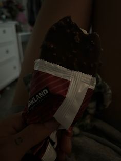 a person holding a bag of chocolate covered candy bar in their left hand while sitting on a bed