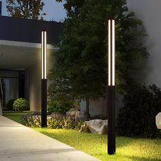 two lights that are on the side of a building near some grass and trees in front of a house