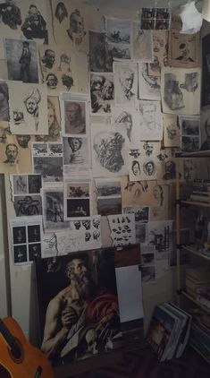 a wall covered in pictures and drawings next to a guitar