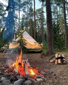 a campfire in the middle of a forest next to a tent with lights on