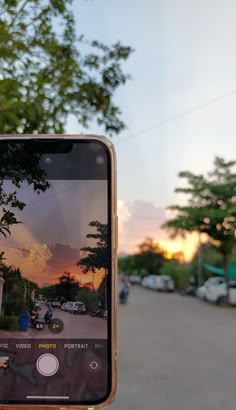 someone holding up their cell phone to take a picture of the sunset on the street