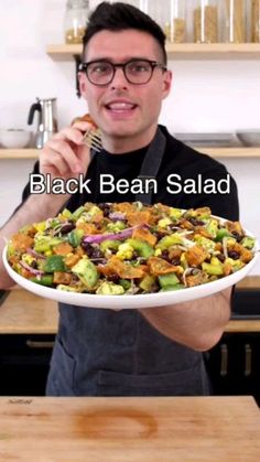 a man holding a plate with a salad on it and the words black bean salad in front of him