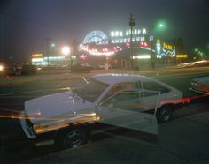 an old car is parked on the side of the road in front of a neon sign