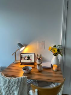 a laptop computer sitting on top of a wooden desk next to a vase with flowers