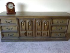 an old dresser with a clock on top of it and carpet in front of the wall