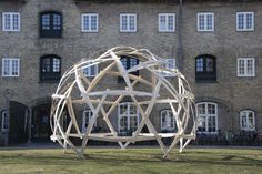 a large wooden sculpture in front of a brick building with windows on the side of it