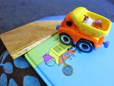 a toy truck sitting on top of a blue table next to a wooden board with a book