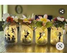 four mason jars with fairy lights and flowers in them on top of a wooden table