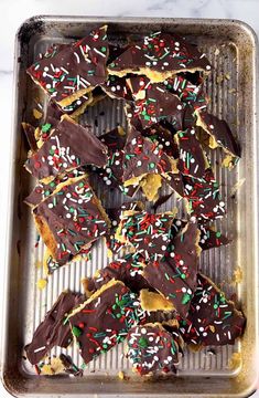 chocolate and sprinkle covered cookies on a baking sheet in a pan with white marble counter top