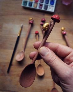 a hand holding two spoons with wooden spoons on the table