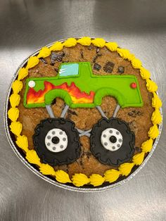 a cake decorated like a monster truck on top of a metal surface with yellow icing