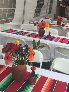 colorful flowers are placed in vases on the tables at an outdoor gathering area for people to sit down