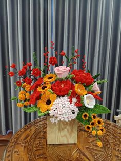 a vase filled with lots of different colored flowers on top of a wooden table next to a metal curtain