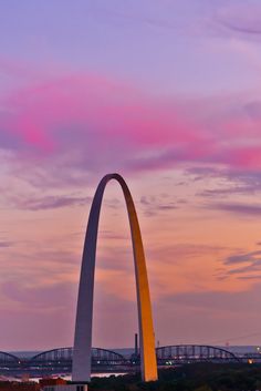 the st louis arch is lit up at dusk with pink clouds in the sky behind it