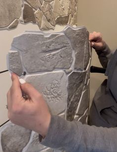 a woman is working on a stone wall with a nail and some scissors in her hand