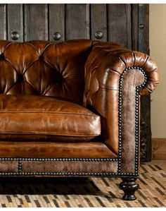 a brown leather couch sitting on top of a hard wood floor next to a wall