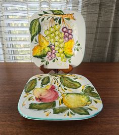 a plate with fruit painted on it sitting on top of a wooden table next to a window