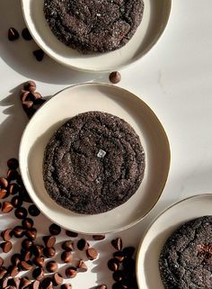 three white bowls filled with cookies and chocolate chips on top of a table next to coffee beans