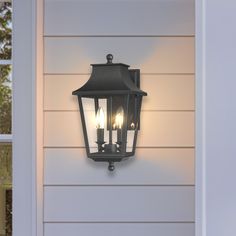 an outdoor wall light on the side of a house with three candles lit up in it