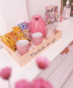 a wooden tray filled with cups and candy on top of a white dresser next to pink flowers