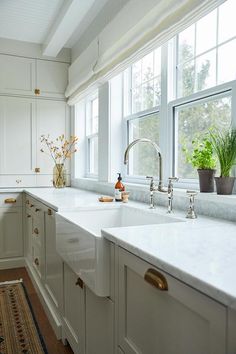 a white kitchen with marble counter tops and gold pulls on the faucet handles