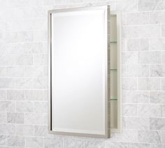 a bathroom mirror mounted to the side of a white tiled wall next to a shelf