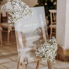 a sign with flowers on it sitting in front of a table at a wedding reception