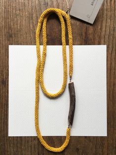 a long yellow rope necklace with a wooden bead and metal clasp on top of a white piece of paper