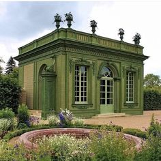 a green building surrounded by lots of flowers and greenery in the middle of a garden