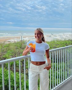 a woman standing on a balcony holding an orange drink