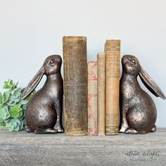 two metal rabbits sitting next to books on a shelf