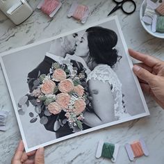 two hands holding a bouquet of flowers next to some sewing needles and scissors on a table