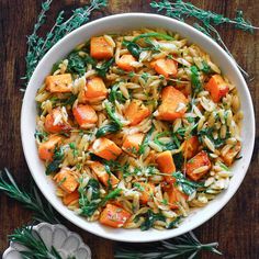 a white bowl filled with pasta and veggies on top of a wooden table