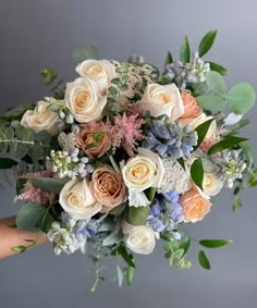 a person holding a bouquet of flowers with greenery on the bottom and blue, white, and pink colors