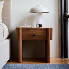 a nightstand with a lamp on top of it next to a bed