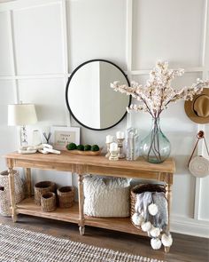 a wooden table topped with baskets filled with flowers next to a mirror and wall hangings