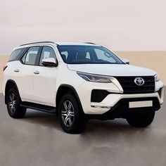 a white toyota fortune is parked in front of a desert wall with sand dunes behind it