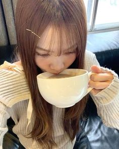 a woman sitting on a couch drinking out of a coffee cup with her eyes closed