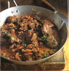 a pan filled with meat and vegetables on top of a wooden table