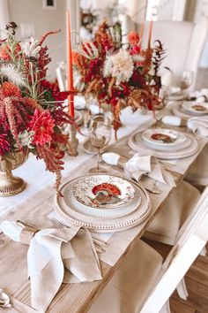 the table is set with plates, silverware and red flowers in glass vases