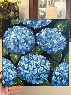 a painting of blue hydrangeas is being held up by someone's hand