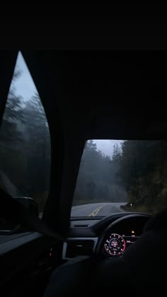 the dashboard of a car driving down a road in the foggy night with trees on both sides