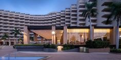 an outdoor swimming pool in front of a large building with balconies and palm trees