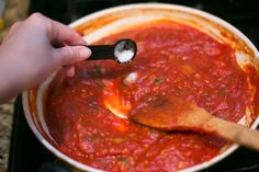 a person spooning sauce into a pot with a wooden spoon