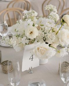 a table with white flowers and place cards on it for the numbers four to seven